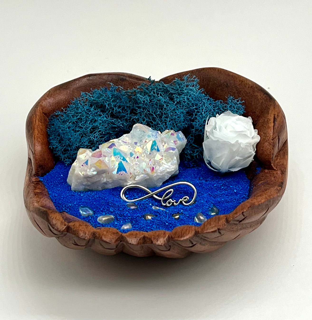 Angel Aura Crystal over a bed of blue sand with a white preserved rose, in a hand carved wood hand bowl
